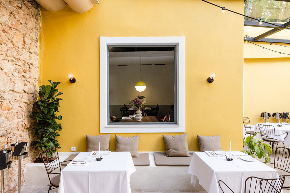 Warmly lit dining space with ochre walls, white tablecloths, and vintage wooden furniture.