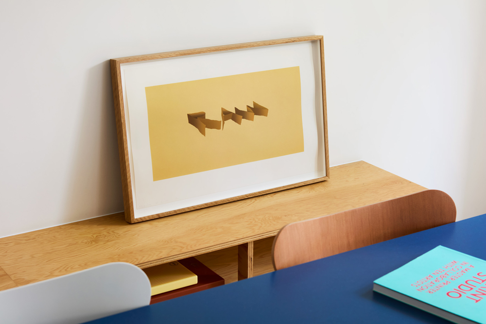 Framed print resting on a timber bench beside the blue dining table.