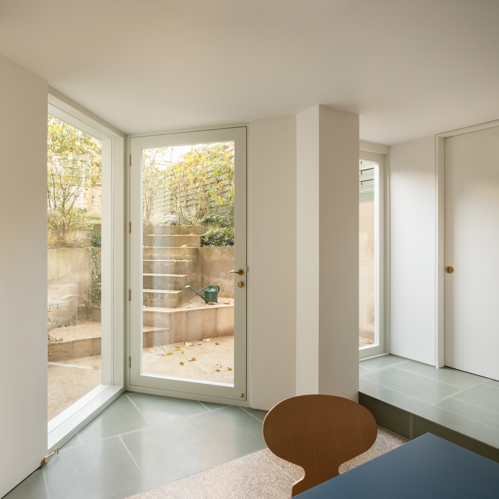 Lower-ground room with angled floor-to-ceiling glazing opening onto stepped garden landscaping.
