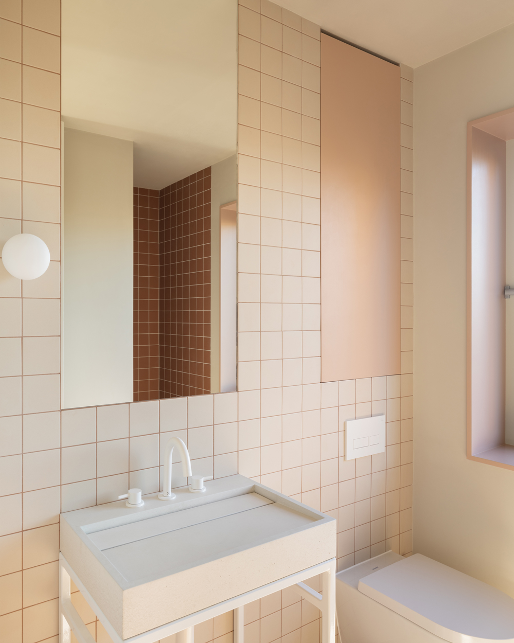 Bathroom with peach and terracotta square tiles, a minimal white basin and soft natural light.