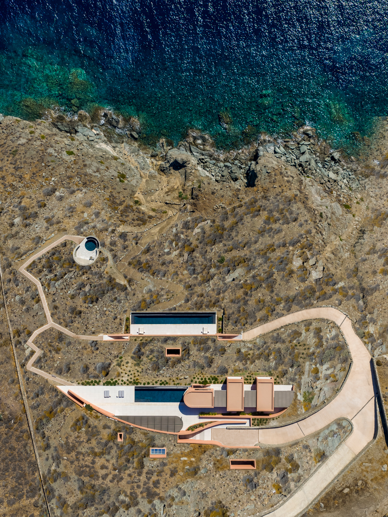 Cliffside architecture of Olen Syros in Syros with minimal volumes integrated into the natural Cycladic landscape.
