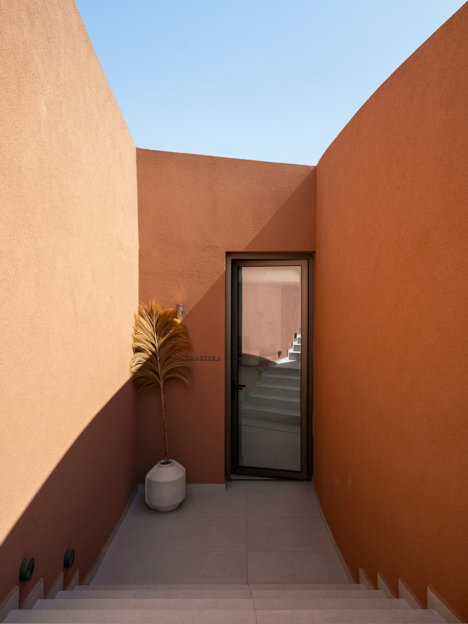 Pathway and built volumes of Olen Syros blending into the sloping landscape of Tria Lagadia in Syros.