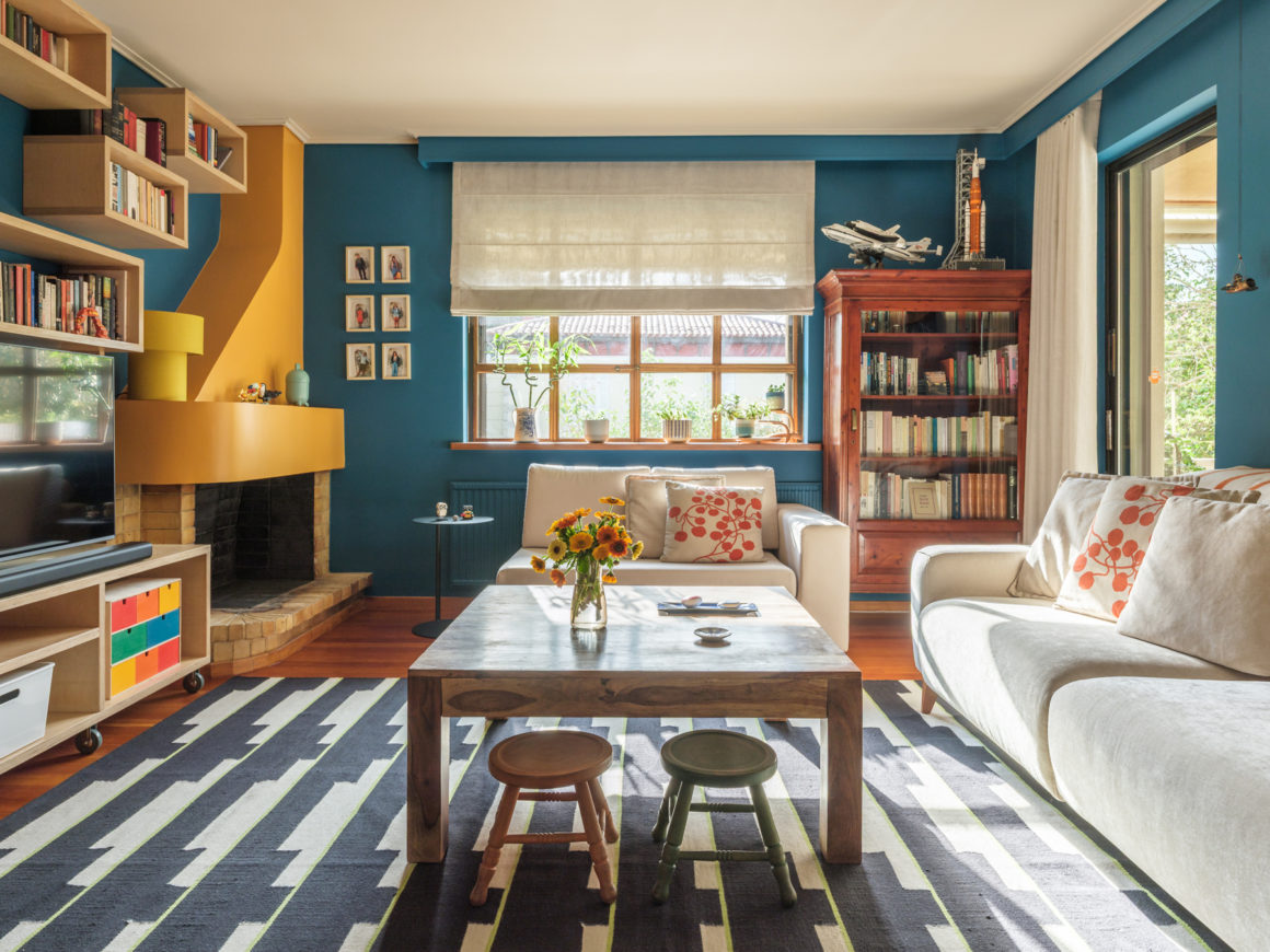 Living area with blue modular sofa, plywood shelving and dining space inside apartment by Ioli Tripodaki