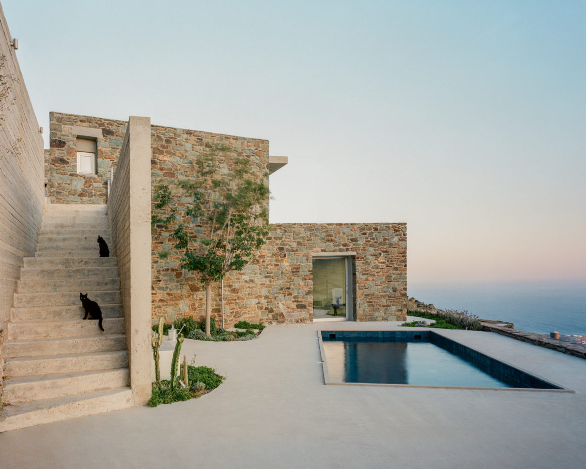 Exterior view of the renovated Tinos house with stone walls, whitewashed volumes and swimming pool overlooking the landscape.