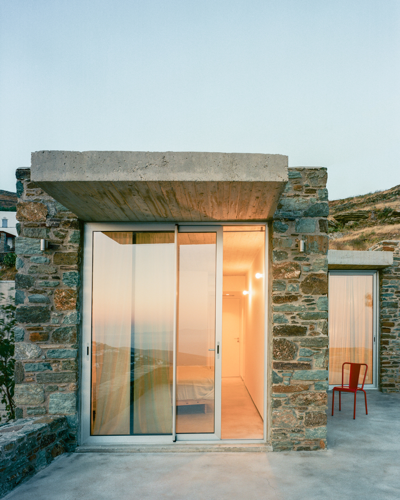 Evening view of the renovated dwelling illuminated against the Tinos landscape.