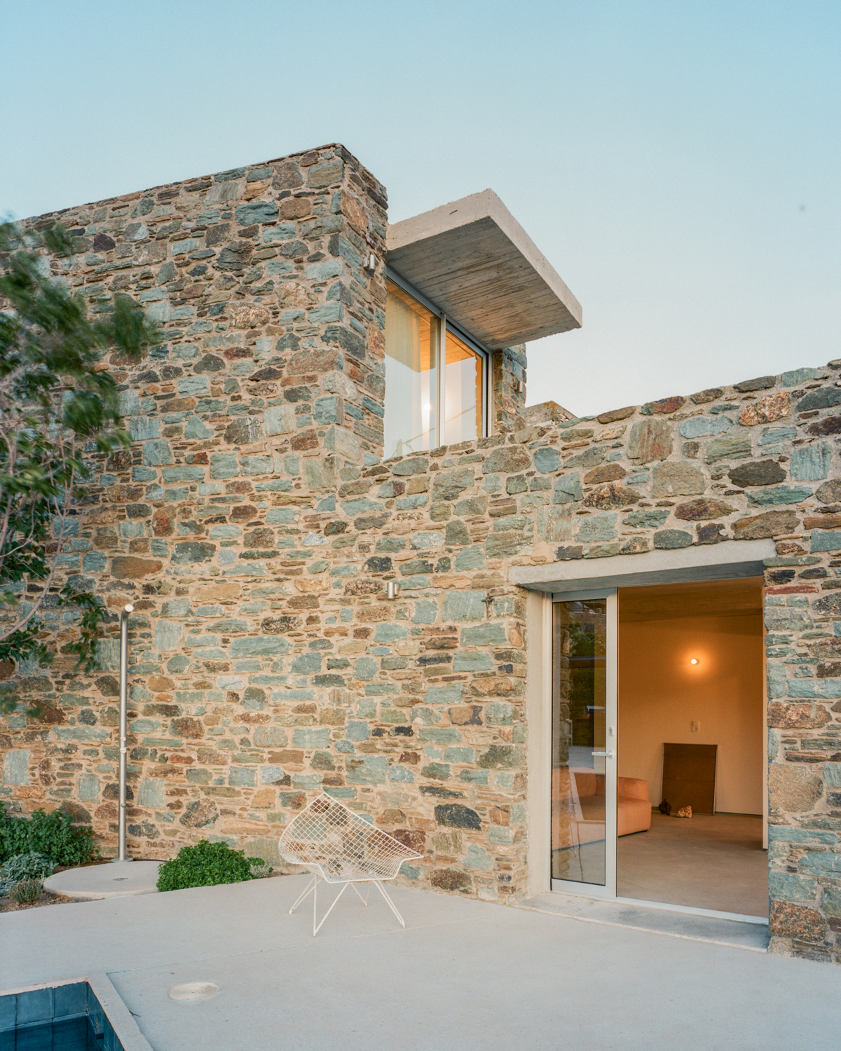 Evening view of the renovated dwelling illuminated against the Tinos landscape.