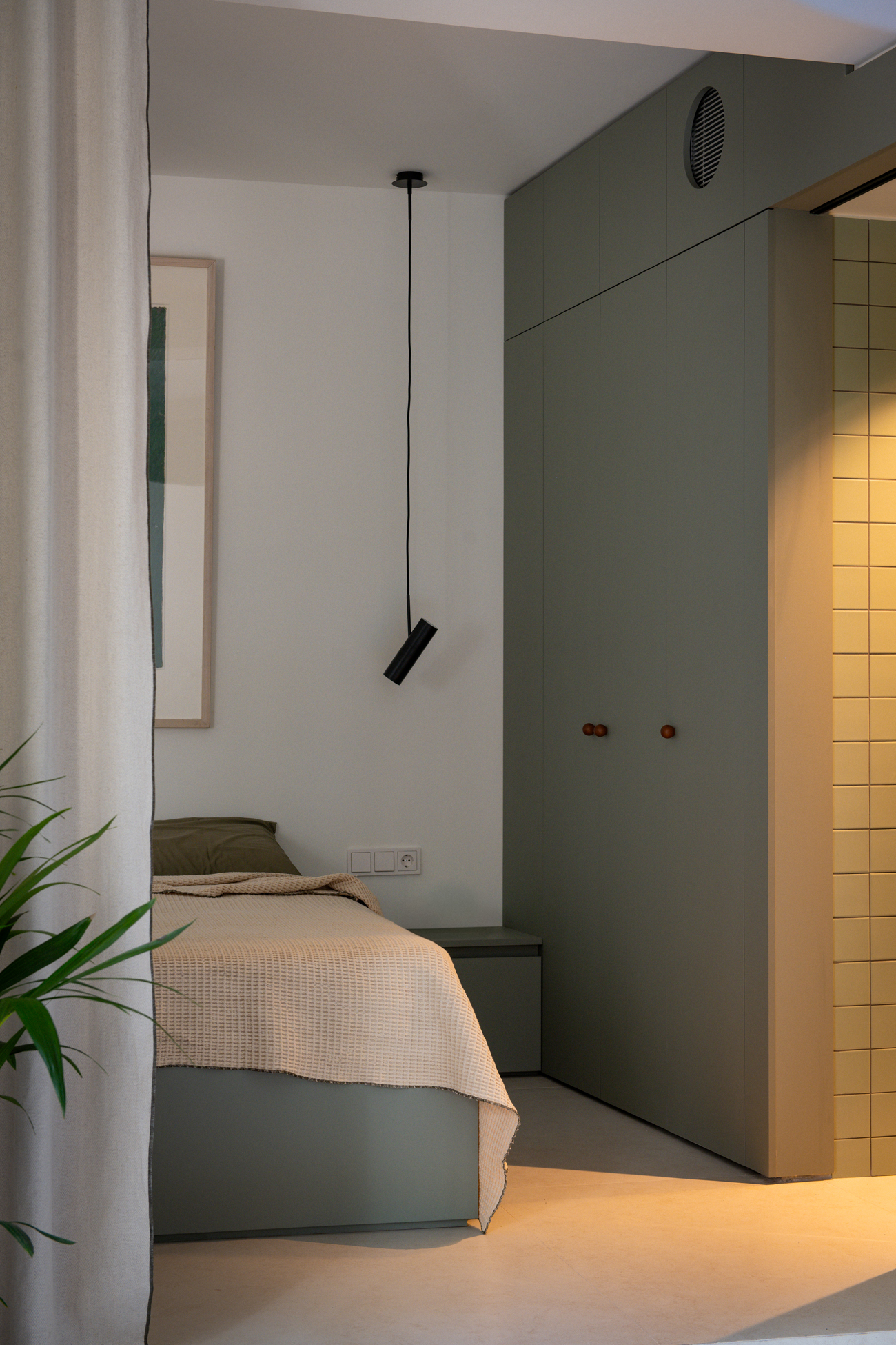Minimal bedroom connected to the open-plan living space and framed by the green cabinetry.