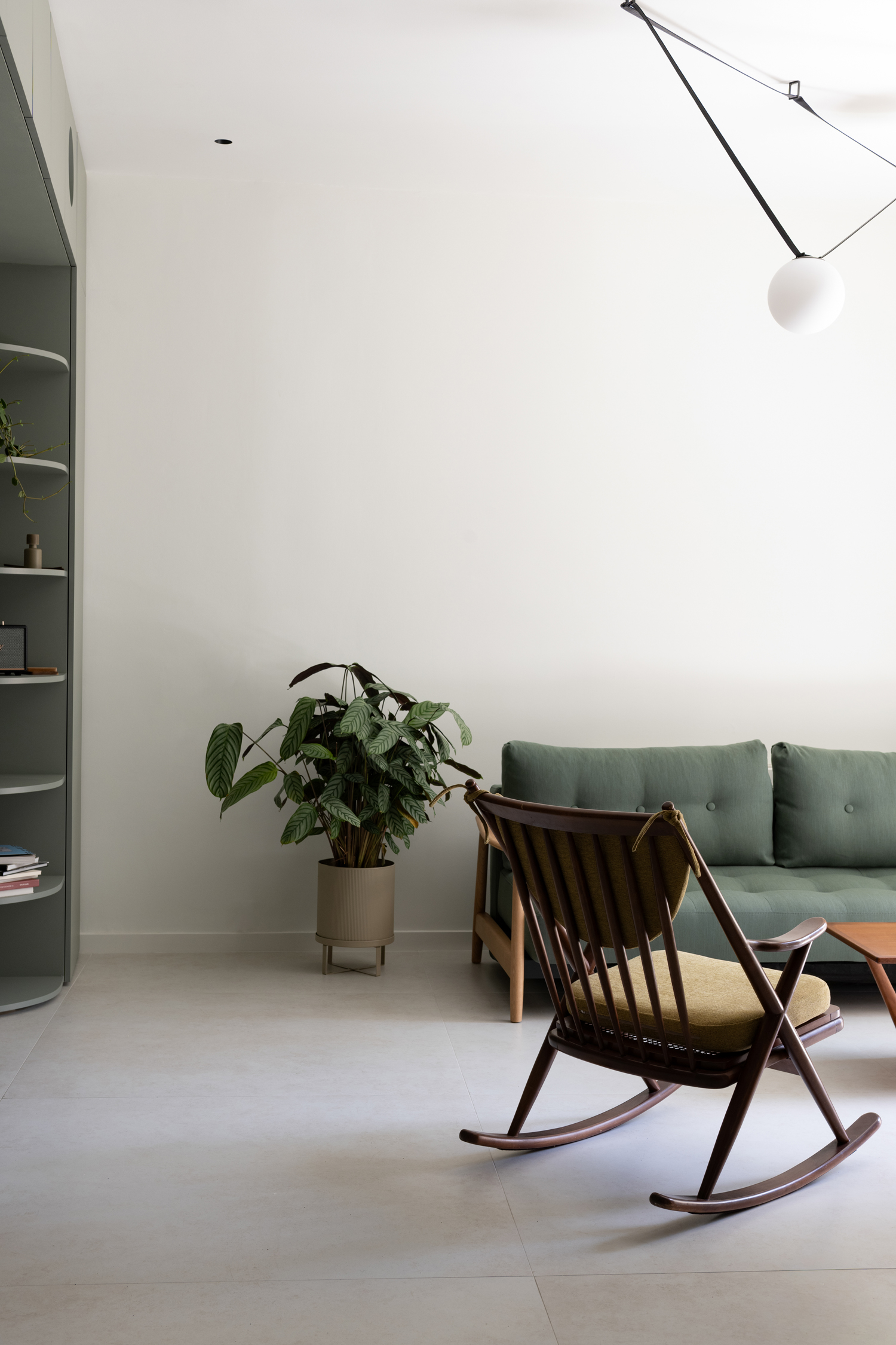 Open-plan living room with green cabinetry, timber flooring and natural light filtering through large windows.