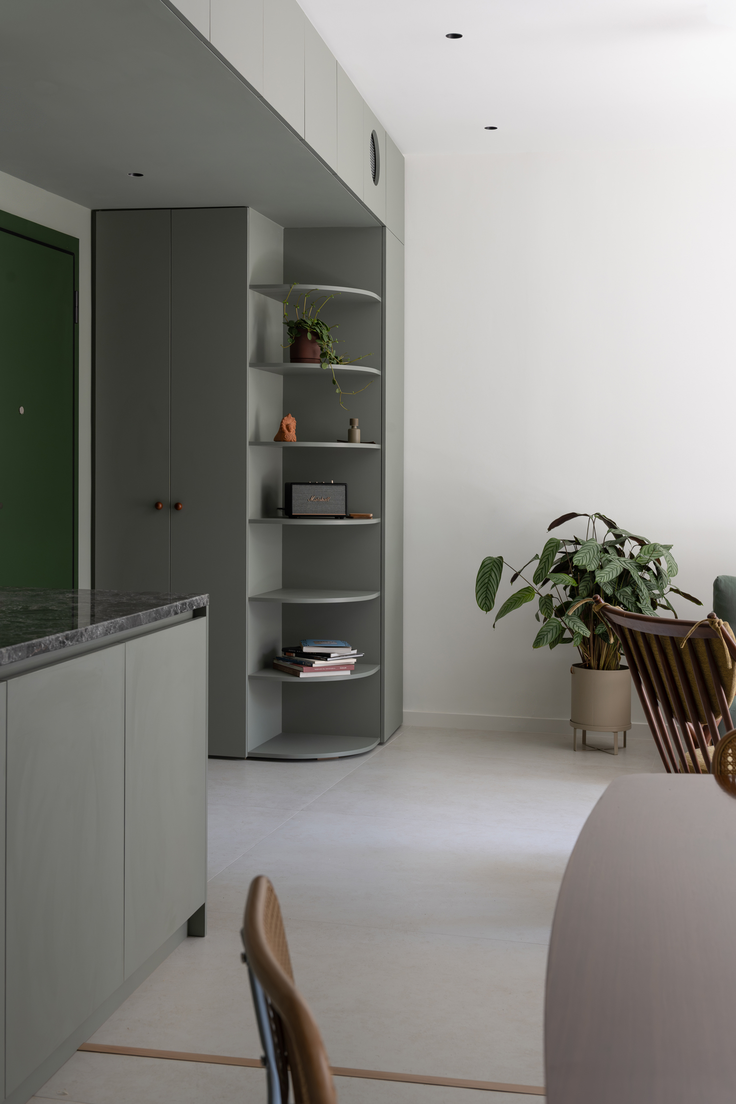 Open-plan living room with green cabinetry, timber flooring and natural light filtering through large windows.